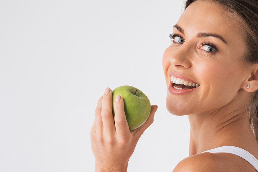 Woman smiling with a green apple in her hand.